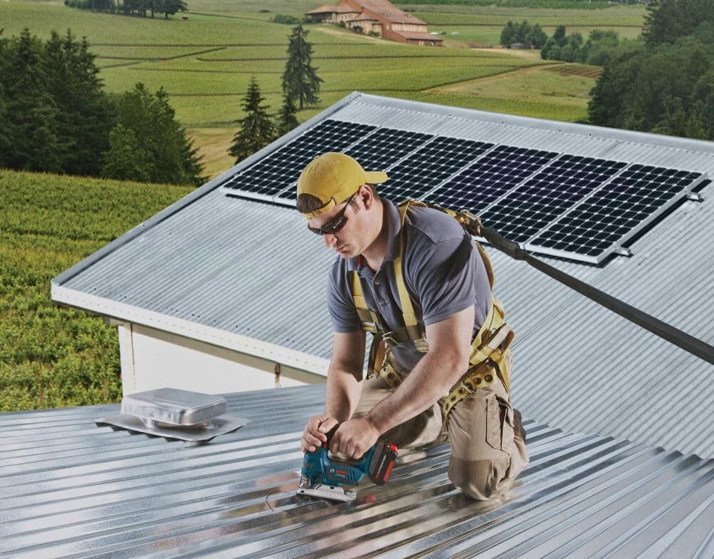 Action shot of a professional tradesman on a rooftop using a Bosch jigsaw to cut corrugated metal roofing.