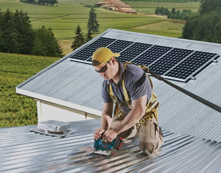 Action shot of a professional tradesman on a rooftop using a Bosch jigsaw to cut corrugated metal roofing.