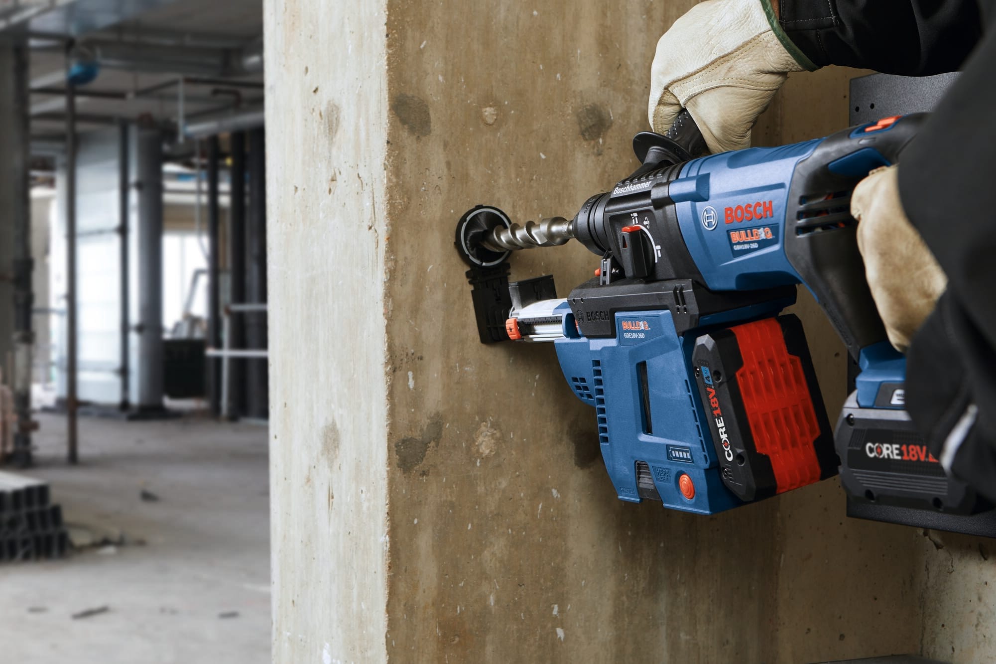 A close-up action view focusing on the mechanical precision of a Bosch Bulldog 18V max rotary hammer drill equipped with a premium carbide-tipped bit from the TCHC9 set. The operator holds the tool with heavy white leather construction work gloves to bore an anchor hole horizontally into a textured concrete barrier panel while utilizing a matching blue HEPA vacuum dust collection shroud.