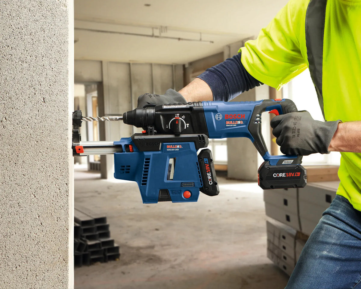 A side-view field shot capturing a contractor operating the Bosch Bulldog cordless 18V rotary hammer drill to bore a clean anchor socket into a masonry structural wall header. The image emphasizes the compact balance of the tool assembly, highlighting the attached HEPA dust extractor box and a precision concrete bit from the TCHC9 kit working through dense stone composite.