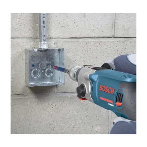 A close-up application shot of an industrial mechanic using a corded Bosch hammer drill to fasten a masonry screw inside a metallic electrical junction box mounted to a concrete block wall. The tool is equipped with the extended steel drive sleeve from the TCHC9 installation kit to drive the fastener securely into a pre-drilled pilot hole.