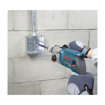 A wider field application shot identical to file TCHC9 7.webp showing an active trade specialist installing structural wiring conduit lines along a commercial masonry basement wall. The contractor utilizes both gloved hands to guide the blue Bosch hammer drill and matching steel sleeve guide attachment from the TCHC9 concrete screw kit to anchor the industrial electrical square box.