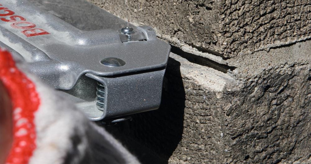 A macro detail shot of the Bosch TG502 guard’s spring-loaded depth adjustment mechanism as it makes contact with a masonry surface, ensuring consistent plunge cut depth.