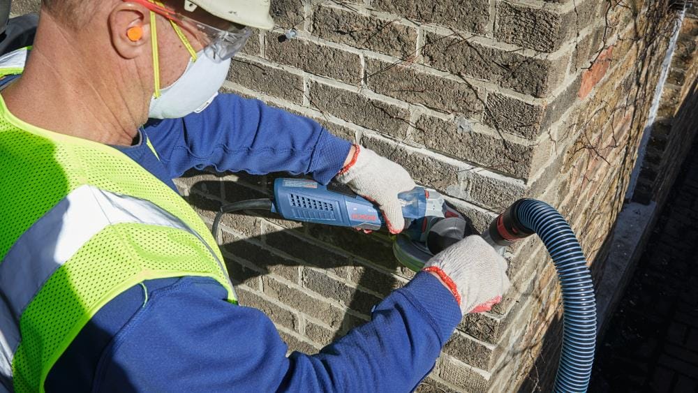 Close-up of a worker guiding a Bosch angle grinder with the TG502 guard along a brick mortar joint, showcasing the precision and control provided by the ergonomic design.