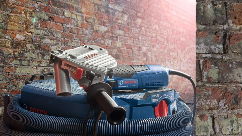 The Bosch TG502 dust guard mounted on a Bosch GWS series angle grinder, connected to a heavy-duty Bosch vacuum hose for professional silica dust management on a brick jobsite.