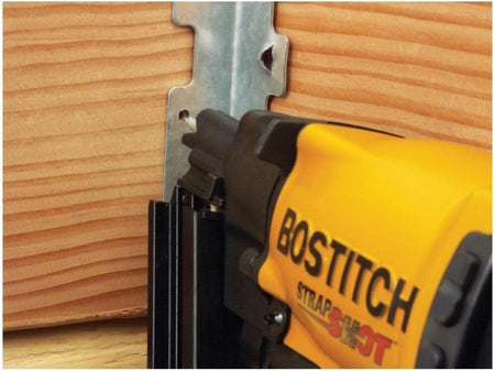 Action close-up showing the Bostitch MCN150 pneumatic nailer fastening a metal hurricane tie to a wooden framing member, emphasizing the compact size and maneuverability in tight structural spaces.