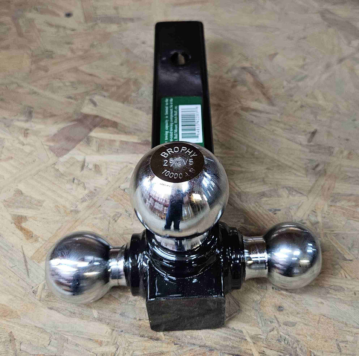 Triple ball trailer hitch mount with three polished metal hitch balls attached to a black rectangular base. The mount includes a green label with the Brophy brand and a towing safety warning. Designed for towing multiple trailer types with different coupler sizes, including 1-7/8", 2", and 2-5/16" balls.