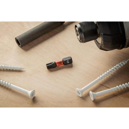 Lifestyle shot of the T30 Torx bit resting on a light wood surface alongside several white construction screws and an impact driver chuck.