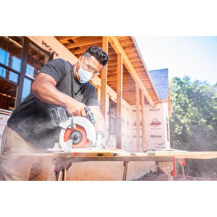 A construction worker wearing a face mask and safety glasses uses a circular saw with the Crescent 10-inch fiber cement blade to cut a piece of siding on an outdoor jobsite.