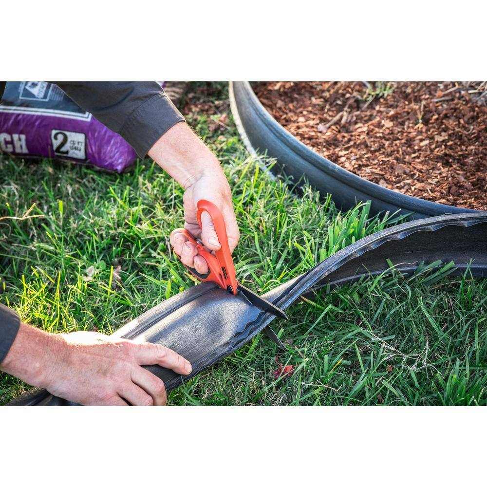 A worker using the Crescent Wiss titanium shears to cut through heavy-duty landscape edging in an outdoor garden setting.