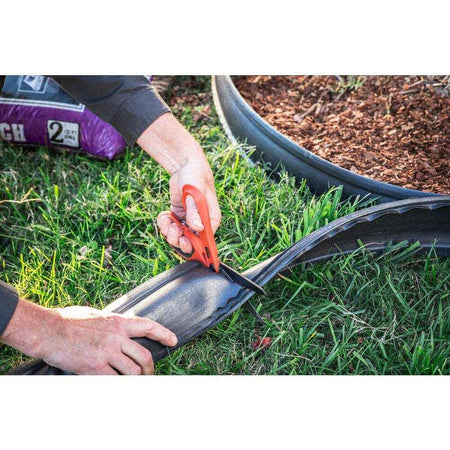A worker using the Crescent Wiss titanium shears to cut through heavy-duty landscape edging in an outdoor garden setting.