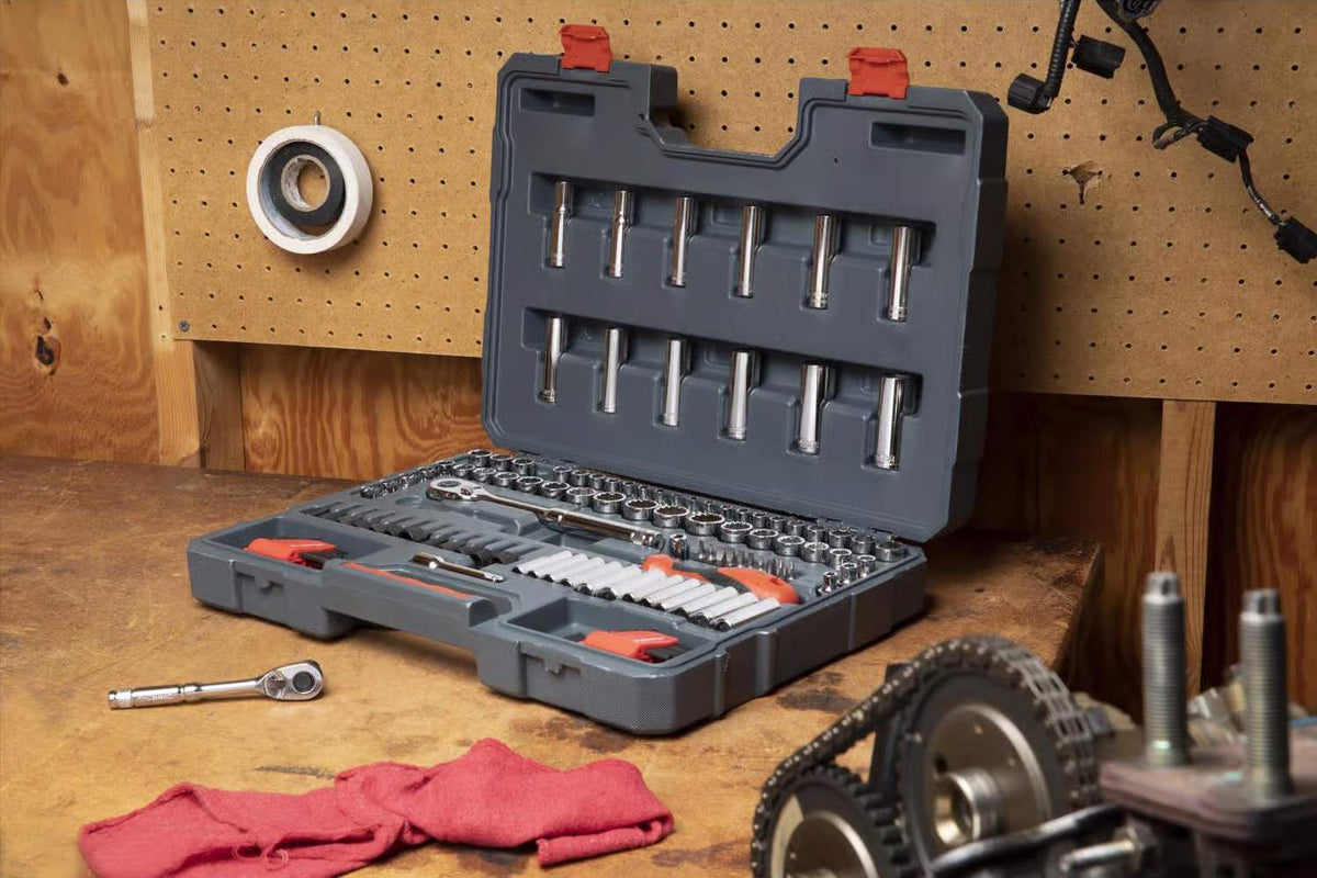 The 121-piece Crescent mechanics tool set opened on a wooden workbench, showcasing the organized sockets, ratchets, and other tools within its gray case, with engine parts and a red cloth nearby