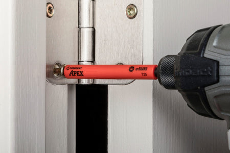 An action shot of the Crescent u-GUARD T25 Torx bit being used with an impact driver to secure a door hinge, demonstrating how the protective sleeve prevents the tool from damaging the surrounding finished surface.