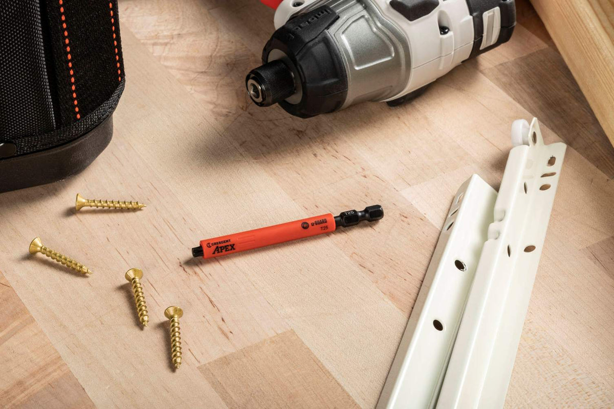 A Crescent u-GUARD T25 impact bit laid out on a light wooden surface alongside gold-finished mounting screws and cabinet hardware, emphasizing its professional use in high-end woodworking and installation projects.