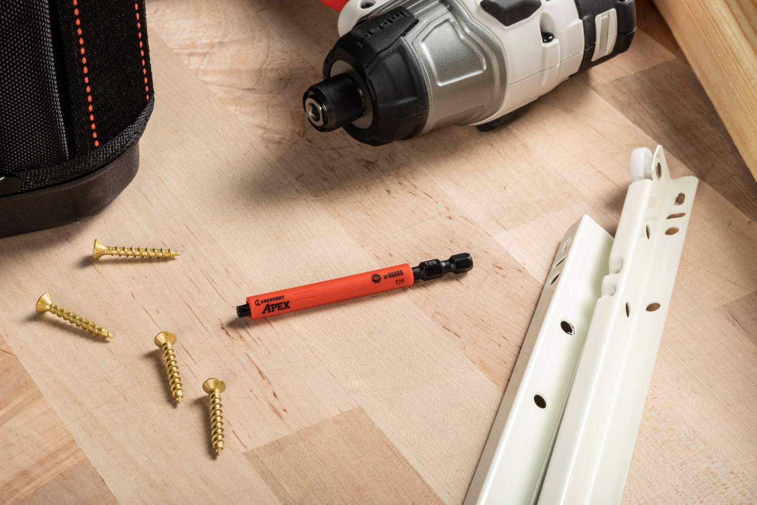 A Crescent u-GUARD T25 impact bit laid out on a light wooden surface alongside gold-finished mounting screws and cabinet hardware, emphasizing its professional use in high-end woodworking and installation projects.