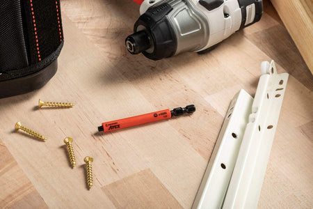 A Crescent u-GUARD T25 impact bit laid out on a light wooden surface alongside gold-finished mounting screws and cabinet hardware, emphasizing its professional use in high-end woodworking and installation projects.