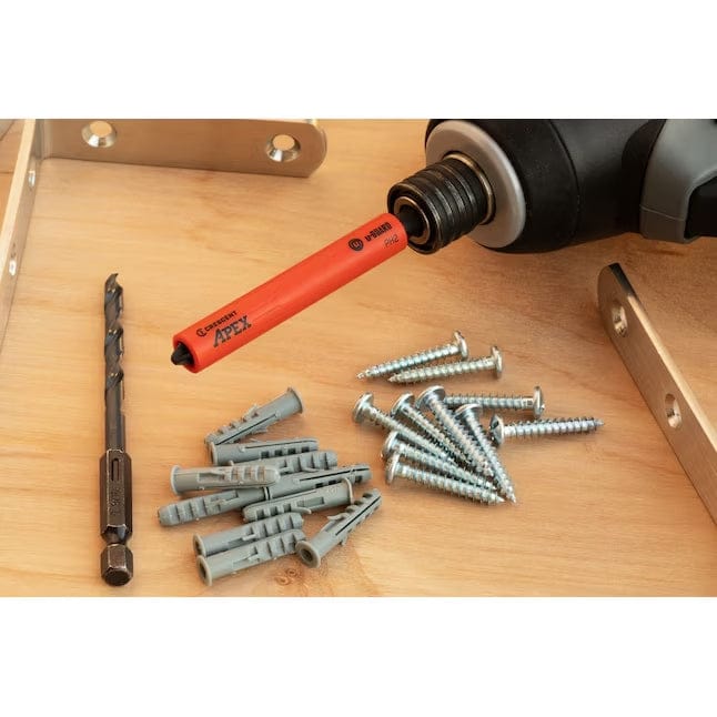 Close-up layout of the Crescent drywall installation set on a wooden surface, showcasing the specialized orange u-GUARD Phillips bit attached to an impact driver alongside the included anchors and drill bit.