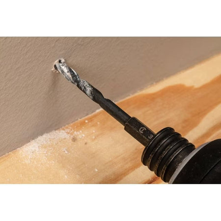 A demonstration of the included 3/16 inch black oxide drill bit creating a precise pilot hole in a drywall surface for secure anchor placement.