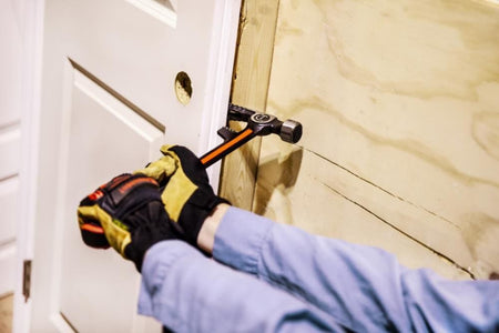 Action shot of a professional using the Crescent steel demo hammer to pry apart a wooden door frame, illustrating the tool's specialized utility for demolition and framing tasks.