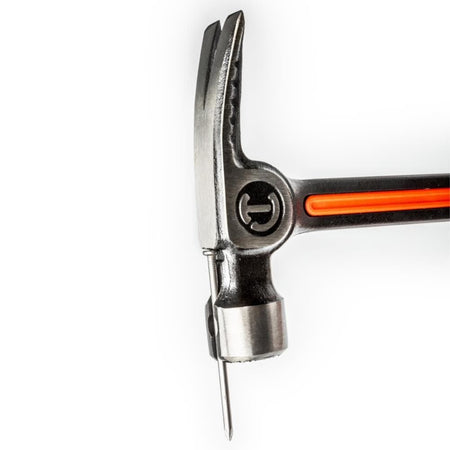 Close-up view of the Crescent 28oz framing hammer head demonstrating the magnetic nail starter feature, securely holding a large framing nail in place for easy one-handed starting.