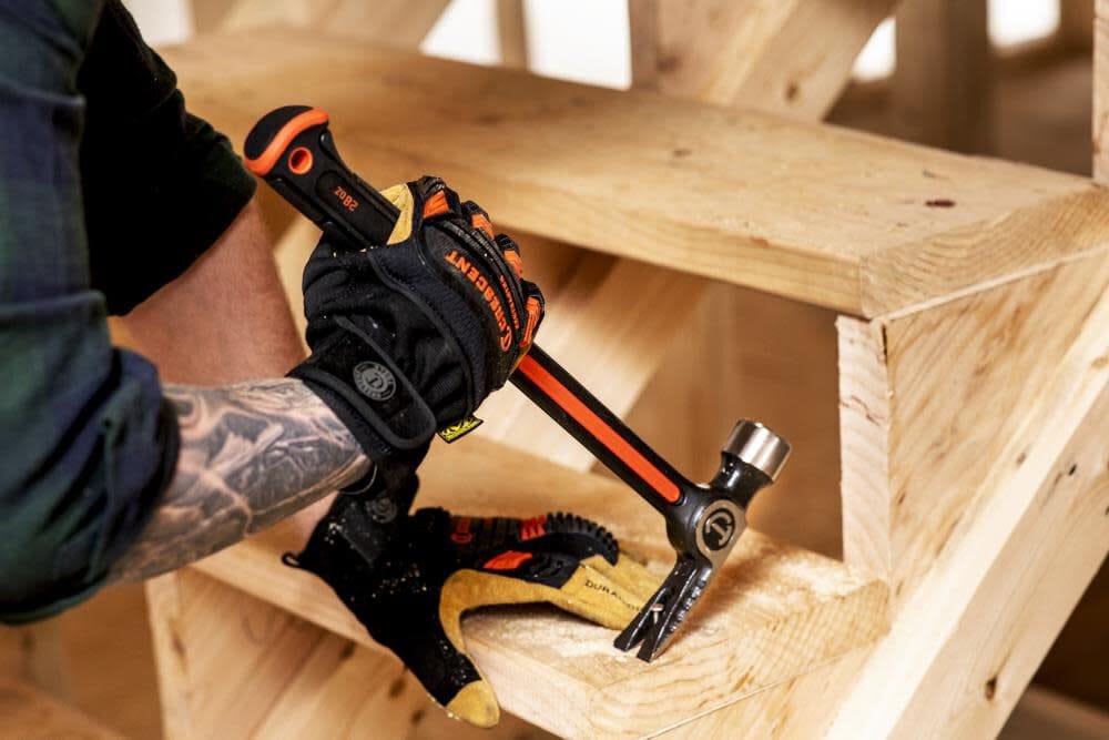Action shot of a professional tradesman using the Crescent 28oz ripping claw hammer to pry a wooden stair tread, demonstrating the tool's heavy-duty utility in a construction environment.