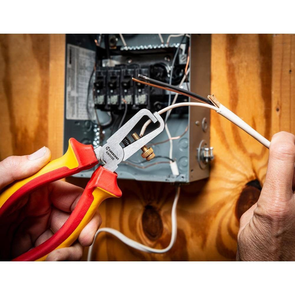A lifestyle action photograph of a professional using the Crescent 6WSVDE insulated wire stripper to remove insulation from a copper wire inside an open electrical panel, demonstrating its precision in high-voltage environments.