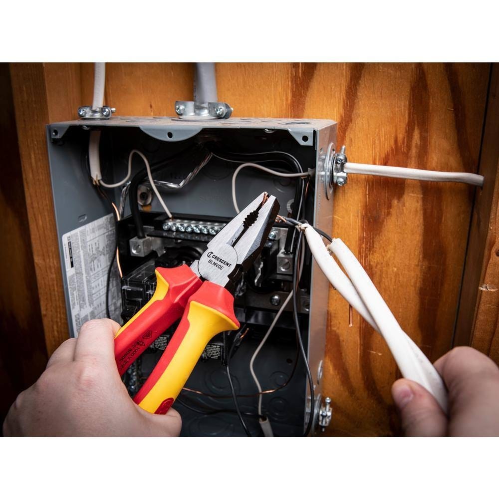 Action shot of a professional using Crescent VDE insulated lineman's pliers to safely strip and manage electrical wiring within a residential junction box, demonstrating the tool's 1000V protection and precision grip.