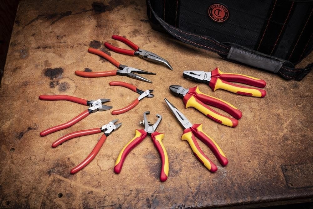 A collection of professional Crescent pliers and hand tools arranged on a wooden workbench, showcasing the 7WSDG wire stripper alongside various long-nose and diagonal cutting pliers.