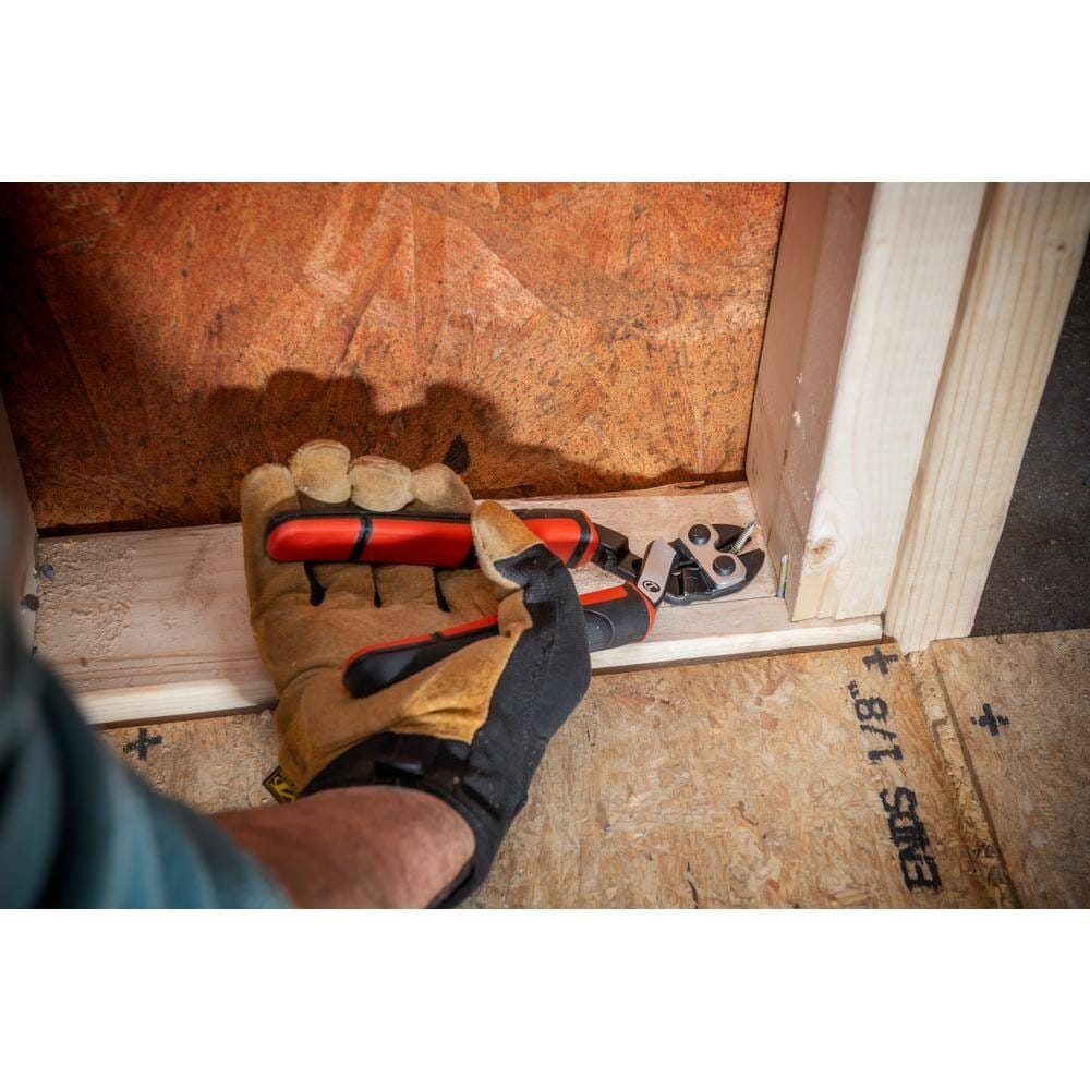 An action shot of a gloved hand using the Crescent angled bolt cutter to perform a flush cut on a nail located in the tight bottom corner of a wooden wall frame.