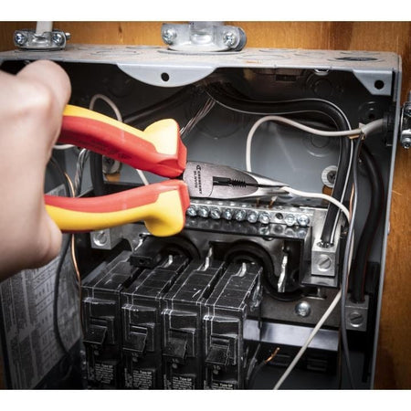 Action shot showing an electrician using the VDE insulated long nose pliers to manipulate electrical wiring inside an open breaker panel