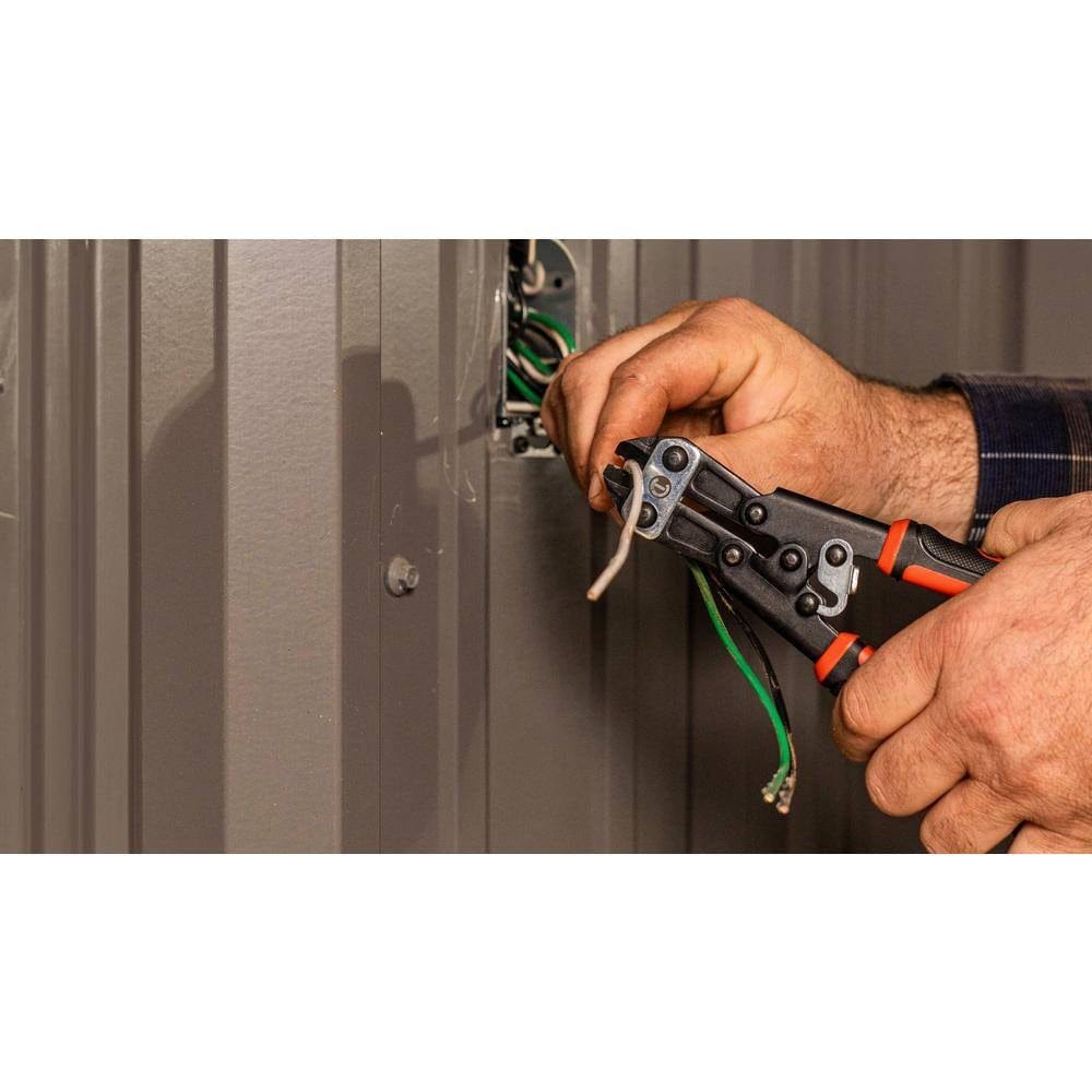 A close-up action shot of an electrician using the Crescent 9-inch multi-purpose wire cutter to precisely trim copper electrical wire near a wall-mounted junction box.