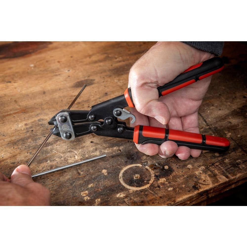 An action photo of a user's hands using the Crescent 9-inch multi-purpose cutter to perform a clean flush cut on a piece of metal wire on a wooden workbench.