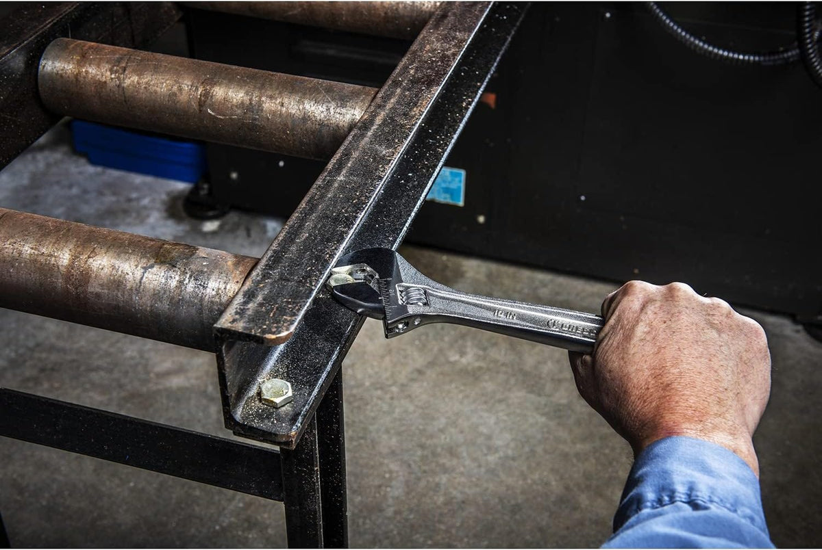 An industrial facility workshop lifestyle photo showing a tradesman using the 10-inch chrome plated alloy steel crescent wrench from the set to firmly tighten a heavy hexagonal structural assembly bolt on a metal roller conveyor frame.
