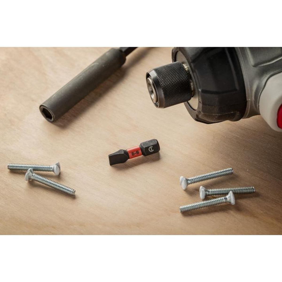 The Crescent 1-inch slotted impact bit displayed on a workshop surface alongside several metal fasteners and a cordless impact driver, illustrating its compact size and professional utility.