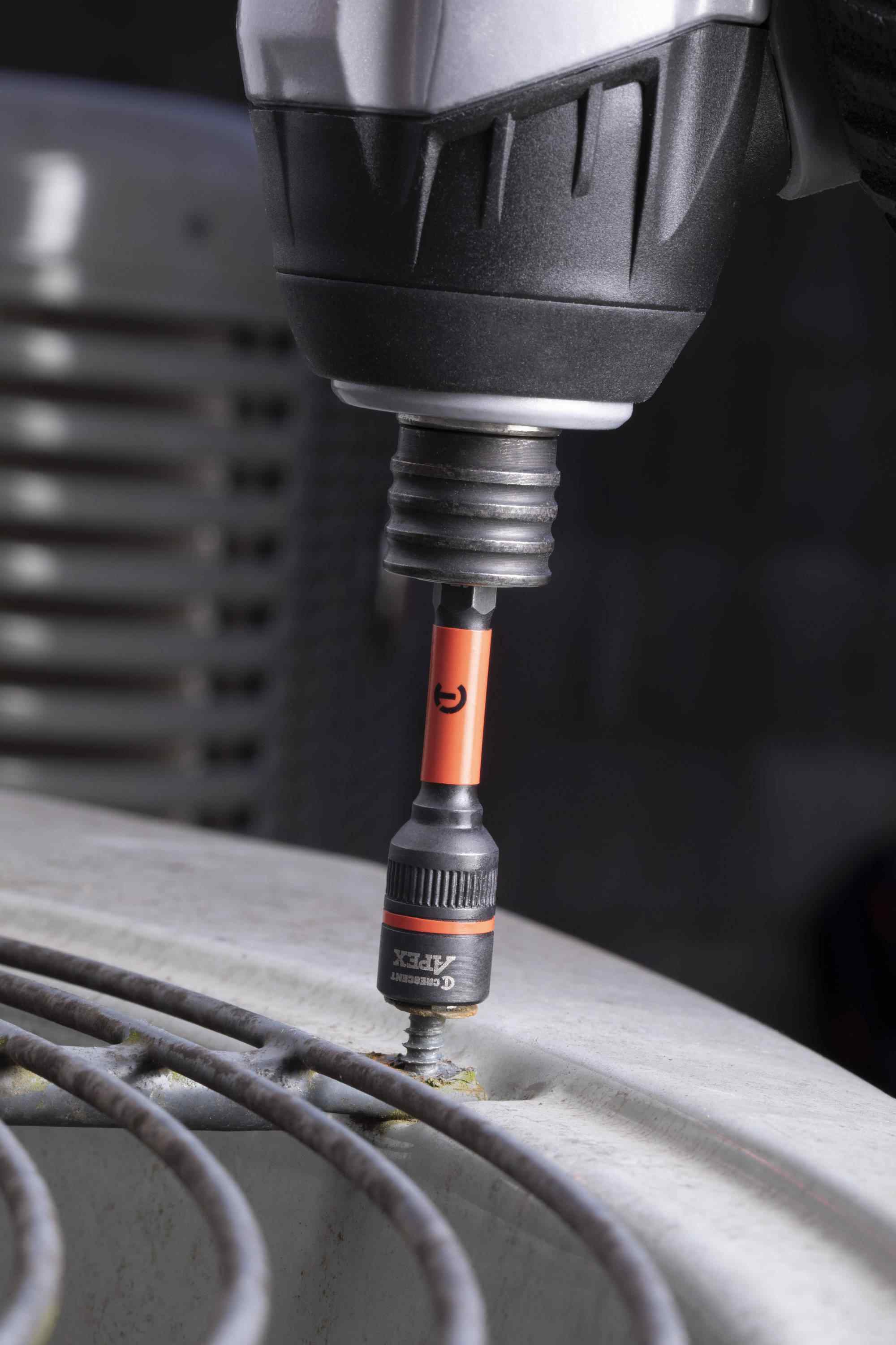 A professional using a power impact driver equipped with the Crescent APEX Bolt Biter 1/4-inch hex shank extractor to effortlessly remove a seized, rusty fastener from the top protective grill of an air conditioning unit.