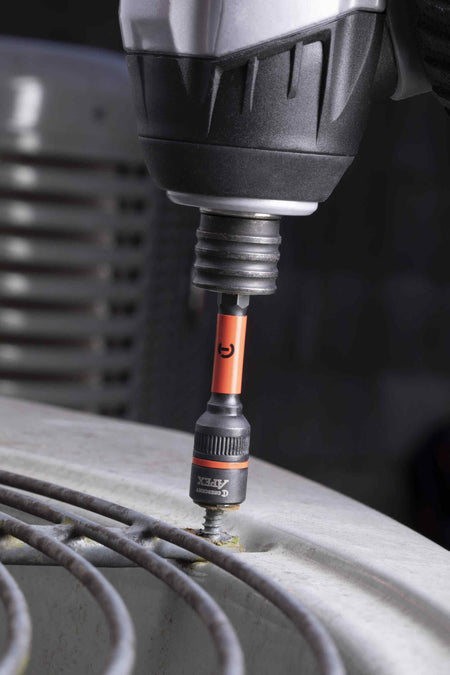 A professional using a power impact driver equipped with the Crescent APEX Bolt Biter 1/4-inch hex shank extractor to effortlessly remove a seized, rusty fastener from the top protective grill of an air conditioning unit.