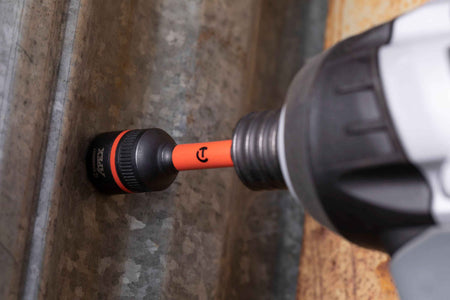 Close-up action shot of the Crescent APEX 1/2-inch Bolt Biter socket fully seated and securely gripping a damaged hex head fastener embedded in galvanized steel siding, being driven by a cordless impact tool.