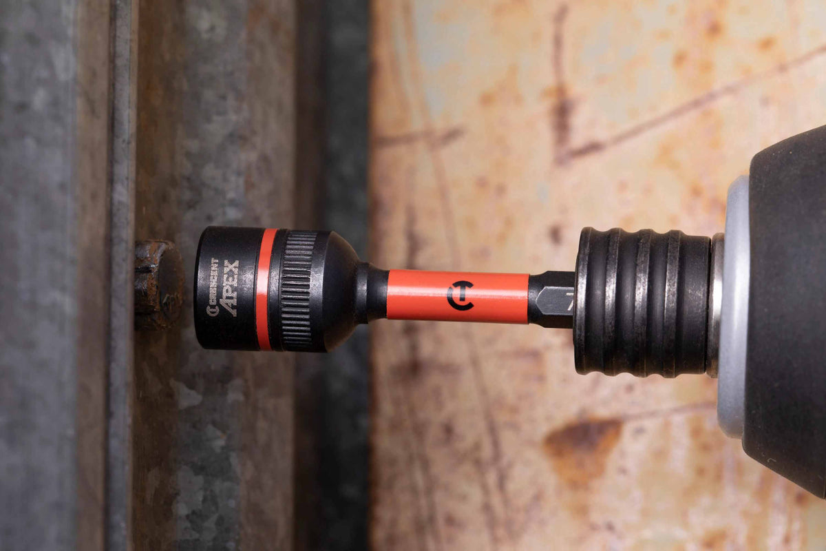 Close-up profile view of the Crescent APEX 1/2-inch Bolt Biter impact nut extractor driver attached to a power tool chuck, actively gripping a damaged and rusted fastener on a galvanized metal surface.