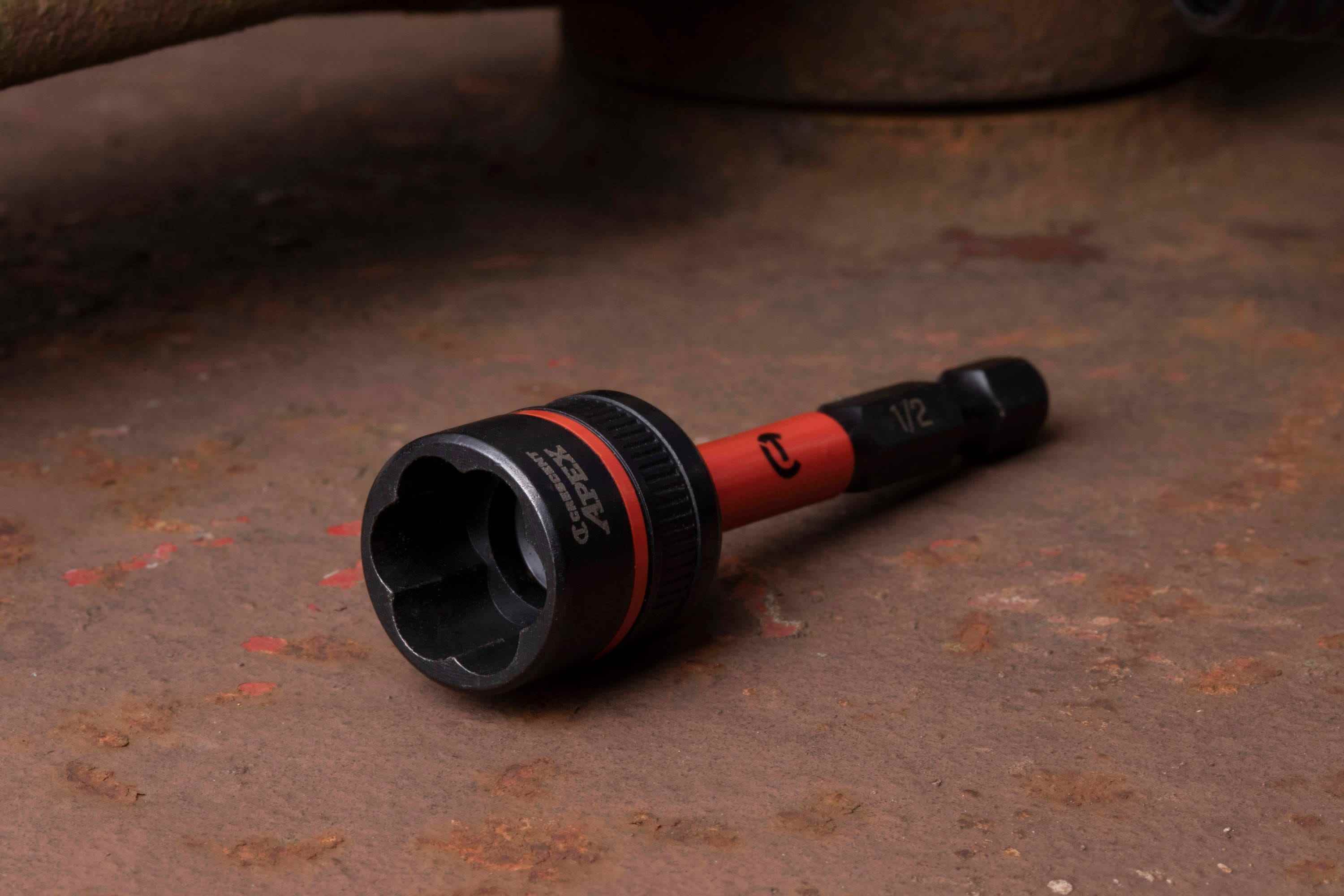 Angled close-up of the Crescent APEX 1/2-inch Bolt Biter lying on rusty steel, prominently displaying the open black oxide socket and its internal tapered flute design engineered specifically for removing damaged rusted fasteners.