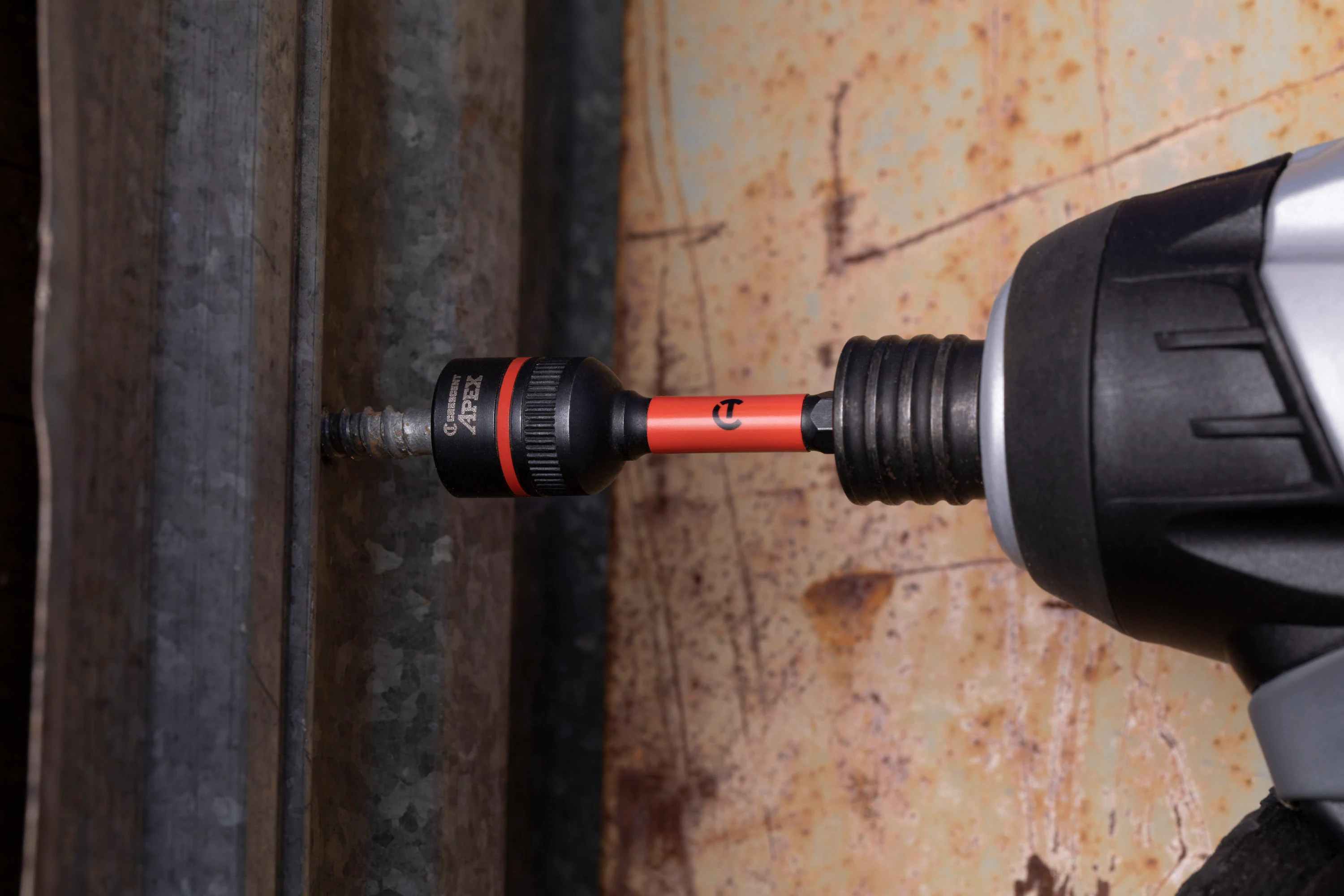 A worker using a power impact driver equipped with the Crescent APEX 1/2-inch Bolt Biter to easily remove a stripped and rusted hex head screw from a piece of galvanized corrugated sheet metal.
