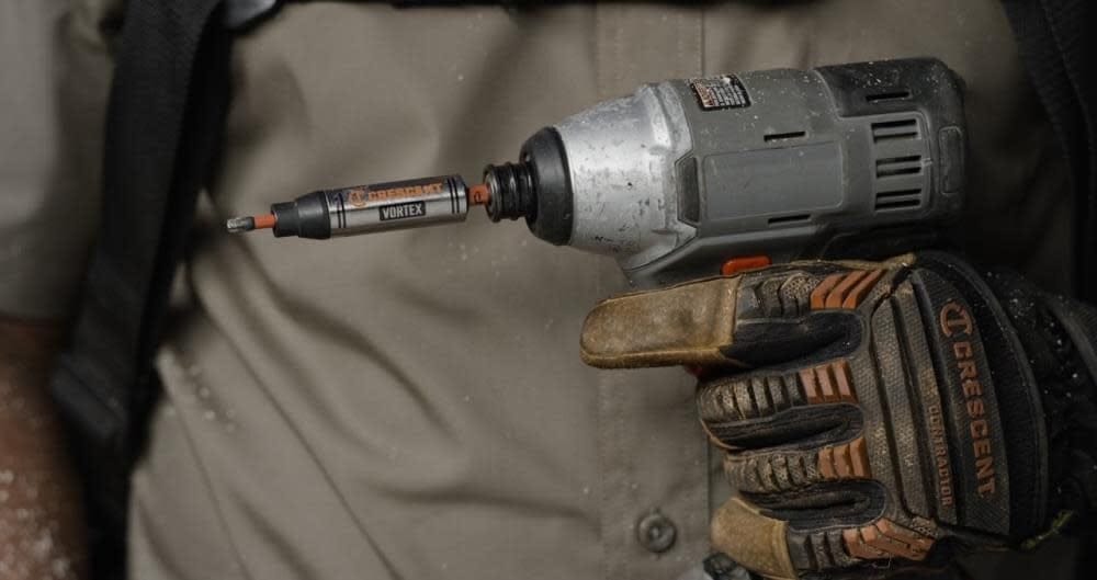 A worker holding a grey impact driver equipped with a Crescent APEX Vortex bit holder, ready for use.