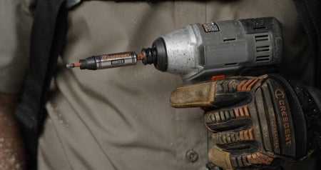 A worker holding a grey impact driver equipped with a Crescent APEX Vortex bit holder, ready for use.