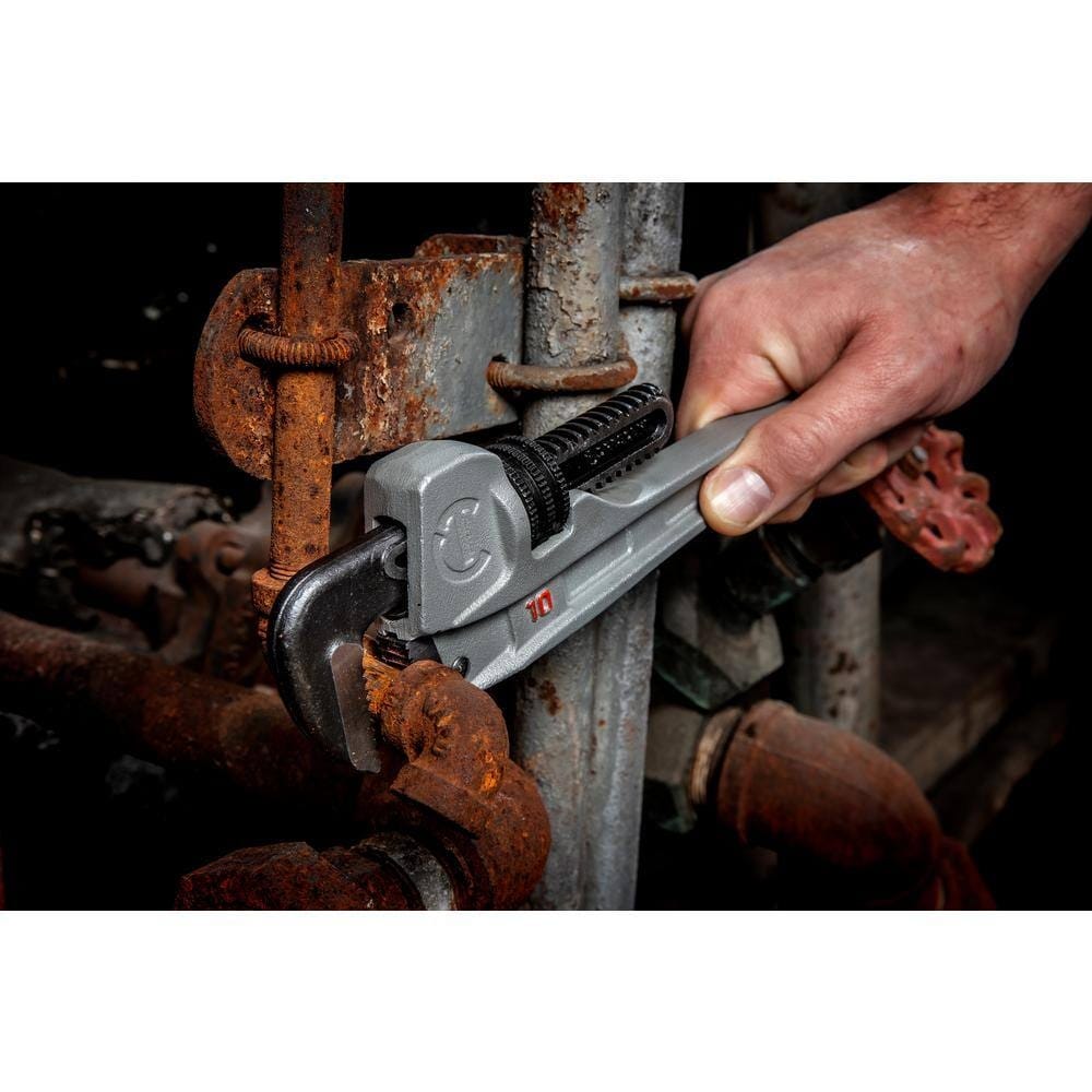 A plumber's hand using the Crescent CAPW10S aluminum pipe wrench to tighten an iron pipe fitting, showcasing the ergonomic grip and precision of the Slim Jaw design.