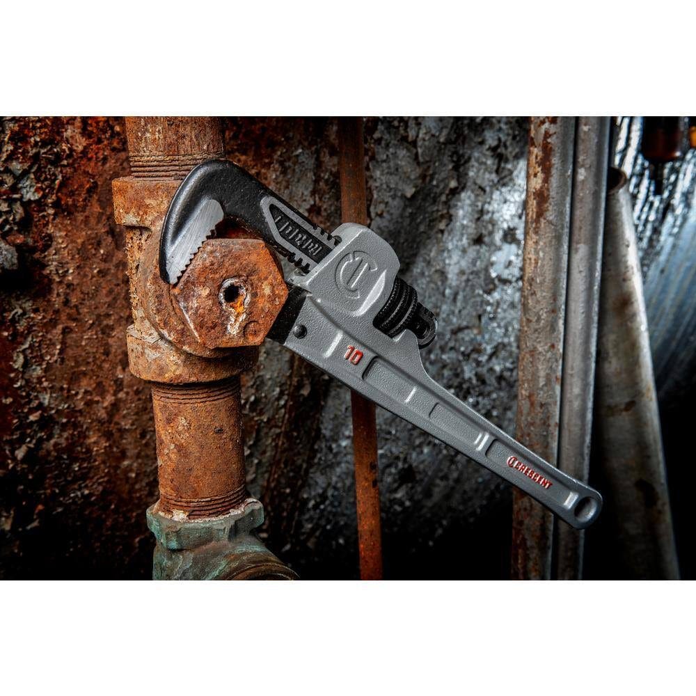 Close-up action view of the Crescent aluminum pipe wrench loosening a heavily corroded hexagonal fitting in a tight industrial plumbing setup.