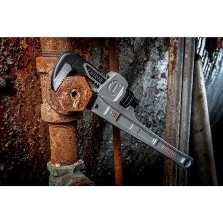 Close-up action view of the Crescent aluminum pipe wrench loosening a heavily corroded hexagonal fitting in a tight industrial plumbing setup.