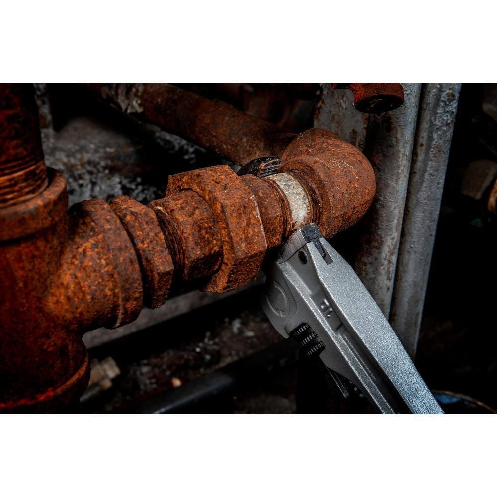 Detail shot of the Slim Jaw profile on the Crescent pipe wrench fitting into a narrow gap to grip a rusted metal pipe in a high-density maintenance environment.