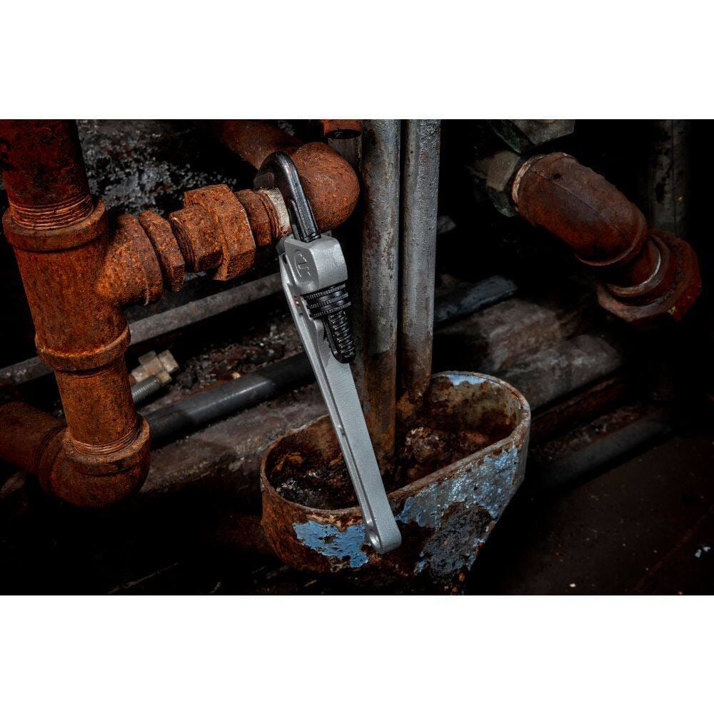 The Crescent 10-inch aluminum pipe wrench hanging vertically from an industrial pipe joint in a dark, cramped maintenance environment to illustrate its Slim Jaw access.