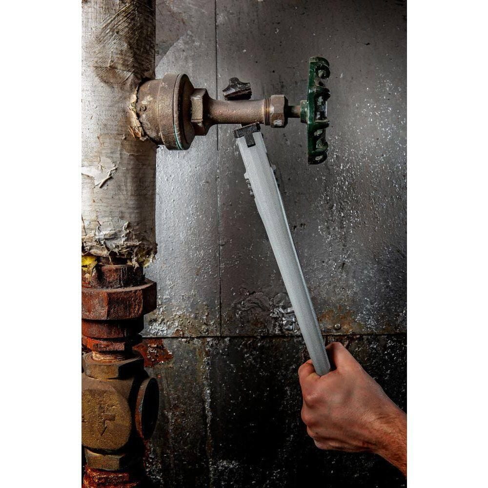 Vertical perspective of a technician using the Crescent CAPW14 pipe wrench to adjust a green valve handle on a high-pressure industrial pipe system, demonstrating the tool's reach and leverage.