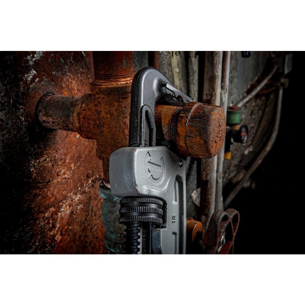 Close-up action shot of the Crescent 14-inch aluminum pipe wrench gripping a heavily rusted iron pipe fitting in a confined, industrial maintenance environment.