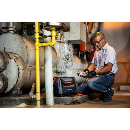 An MRO technician kneeling next to an industrial boiler using the Crescent 14-inch pipe wrench and a professional tool bag to perform routine maintenance.